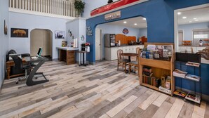 A spacious room with a herringbone floor, a dining area with a wooden table and chairs, a kitchen area, and a loft with a railing.