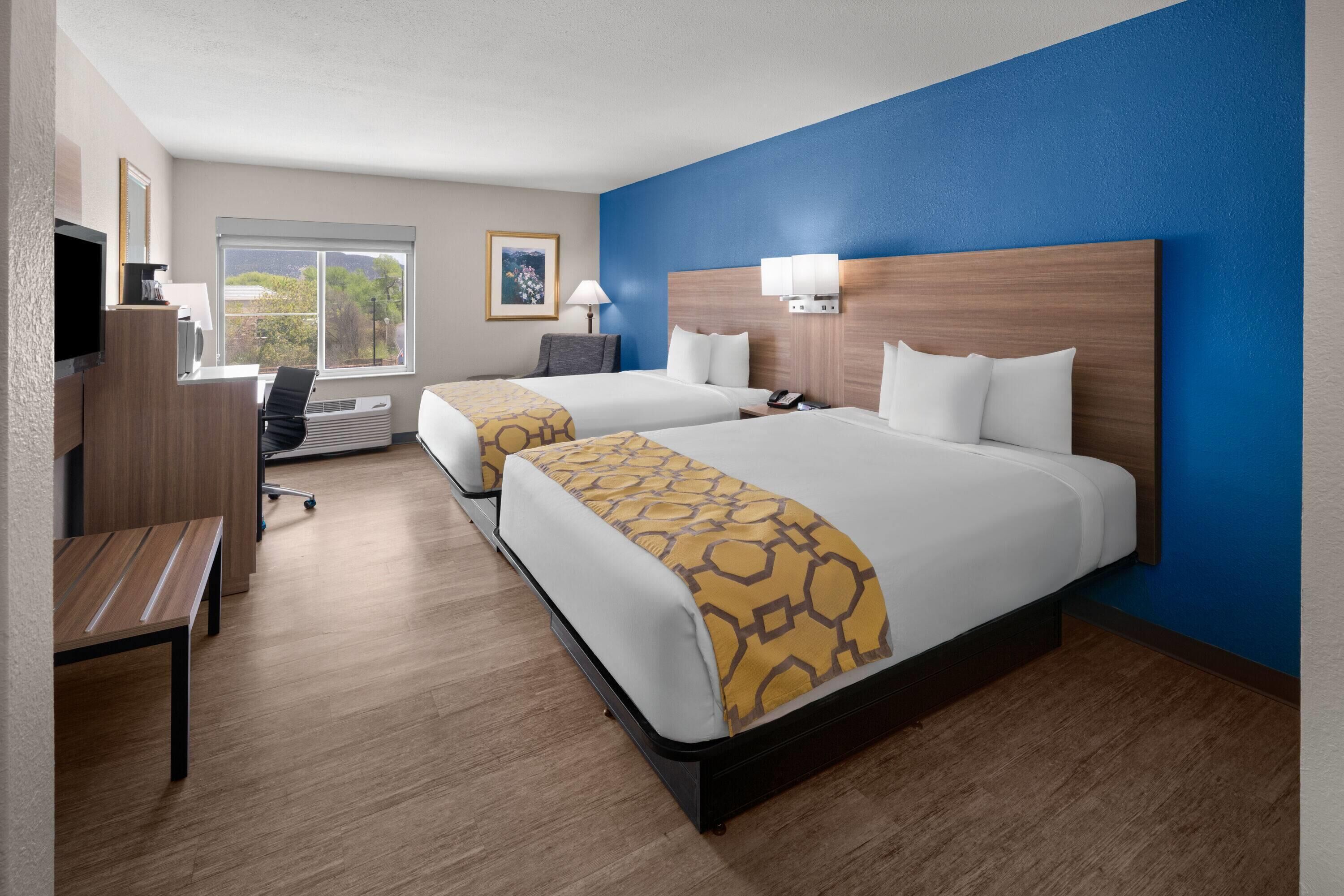 A hotel room with two beds, a desk, a chair, a TV, and a window with a view.