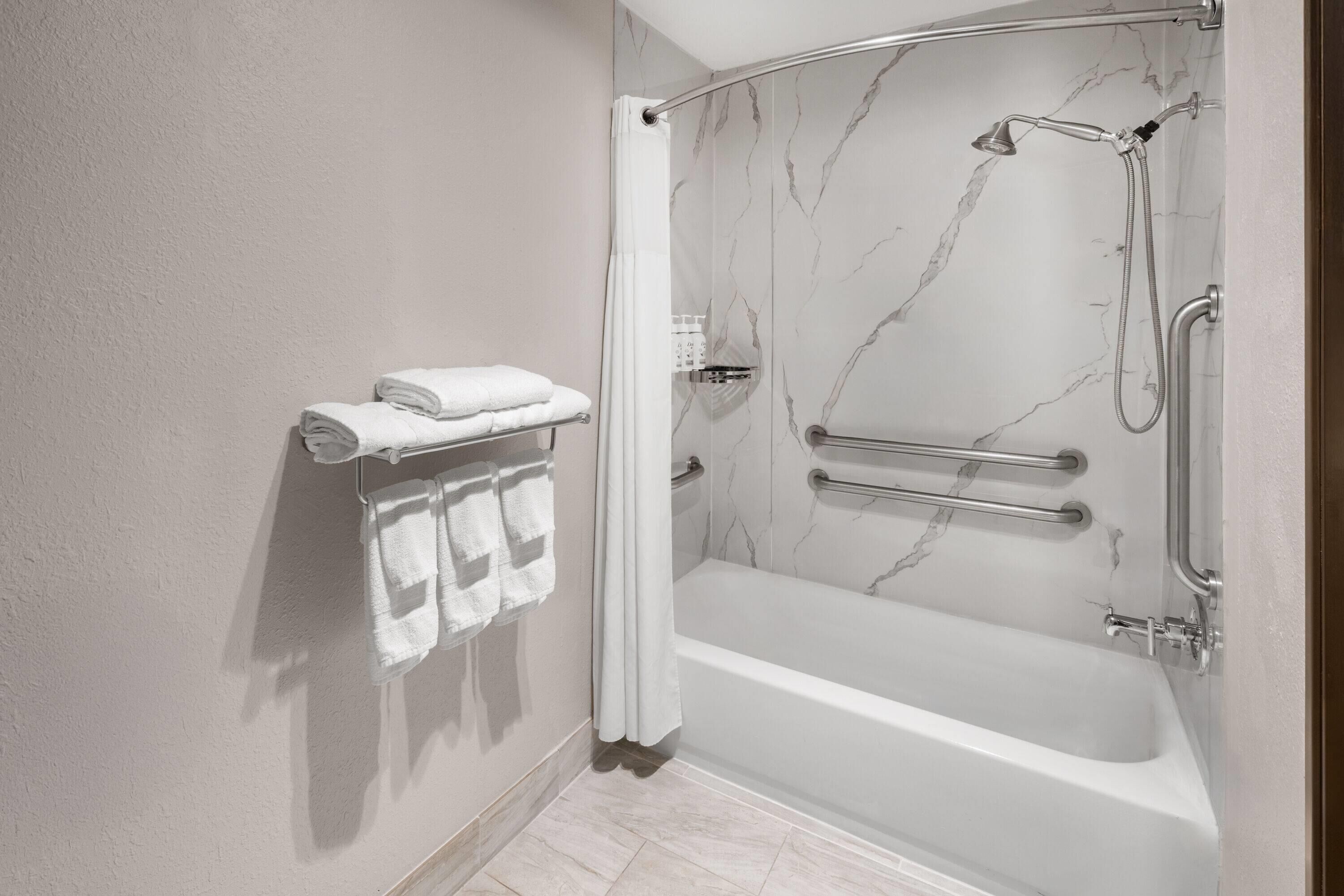 A shower with a glass door, a bathtub, and a towel rack with folded towels.