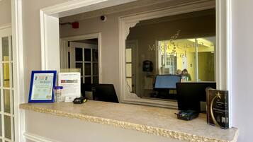 Un comptoir d’accueil d’hôtel avec un ordinateur, un téléphone et un certificat encadré.