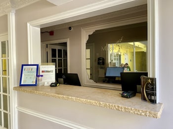 A reception desk with a coffee machine, framed pictures on the wall, and a potted plant. at Magic Castle Hotel