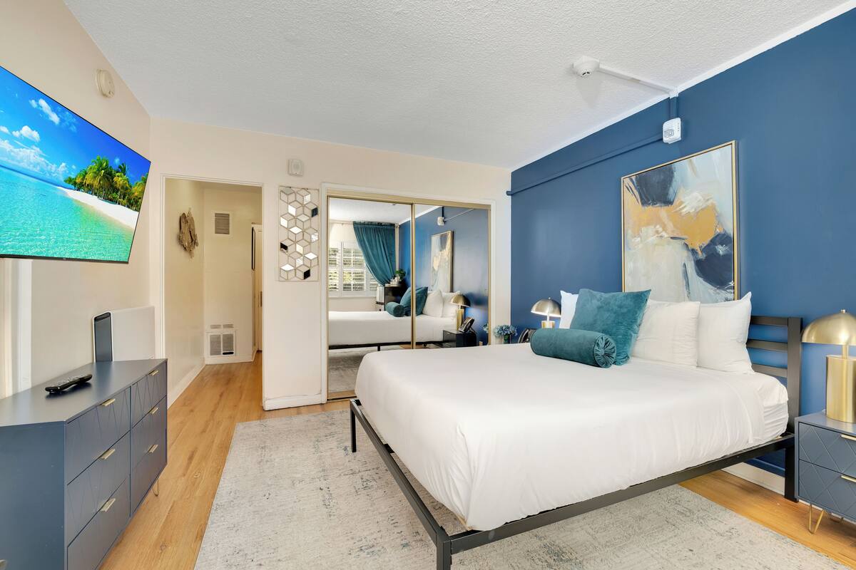 A modern bedroom with a bed, bedside tables, a TV, and a painting.
