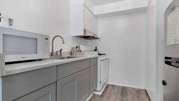 A modern kitchen with grey cabinets, a white countertop, a microwave, a sink, and a stove.