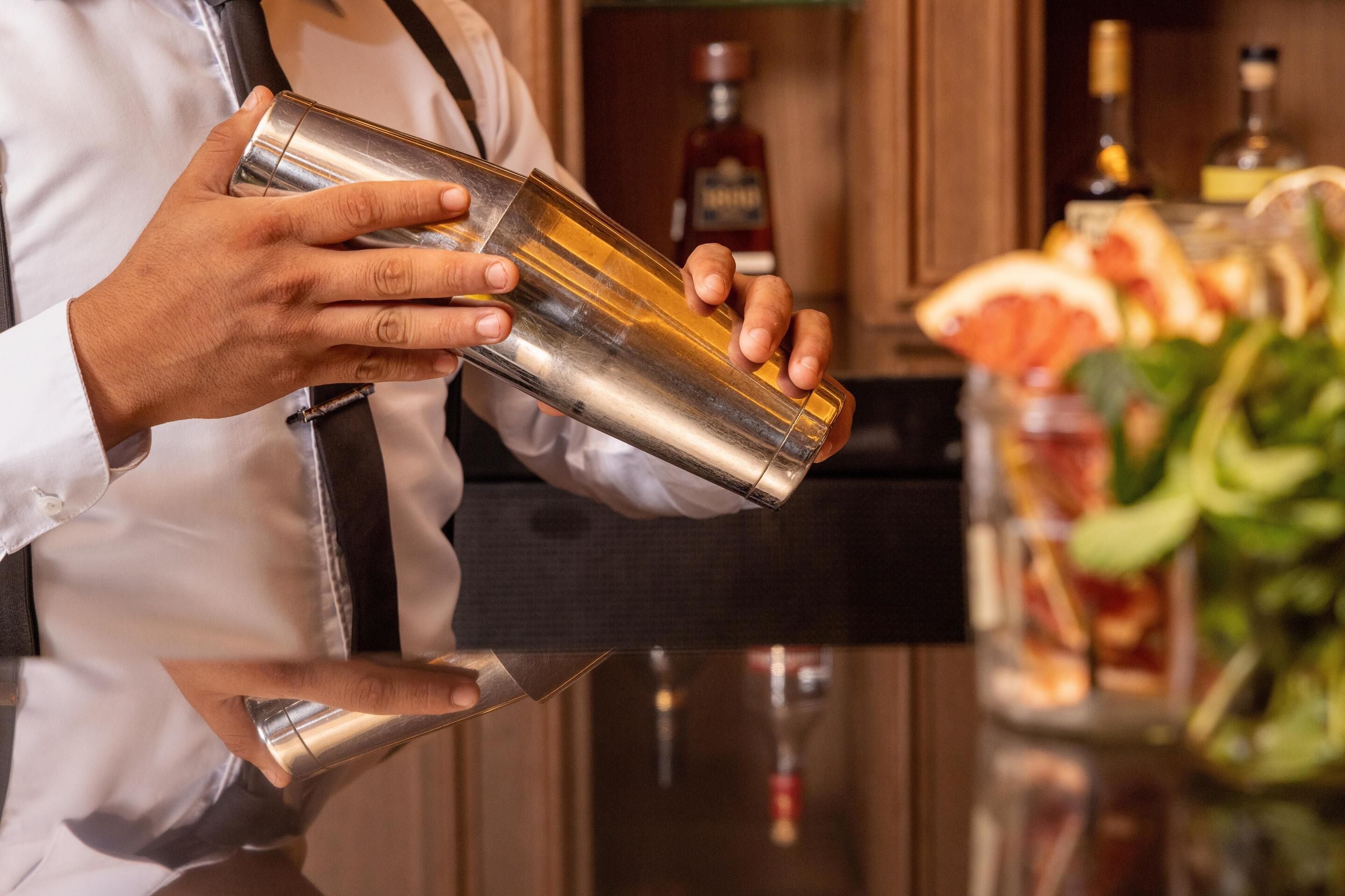 Een barman bereidt een drankje toe met een cocktailshaker en een fles drank.