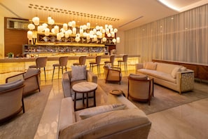 A modern lounge area with a bar, sofas, and chairs arranged around a central coffee table.