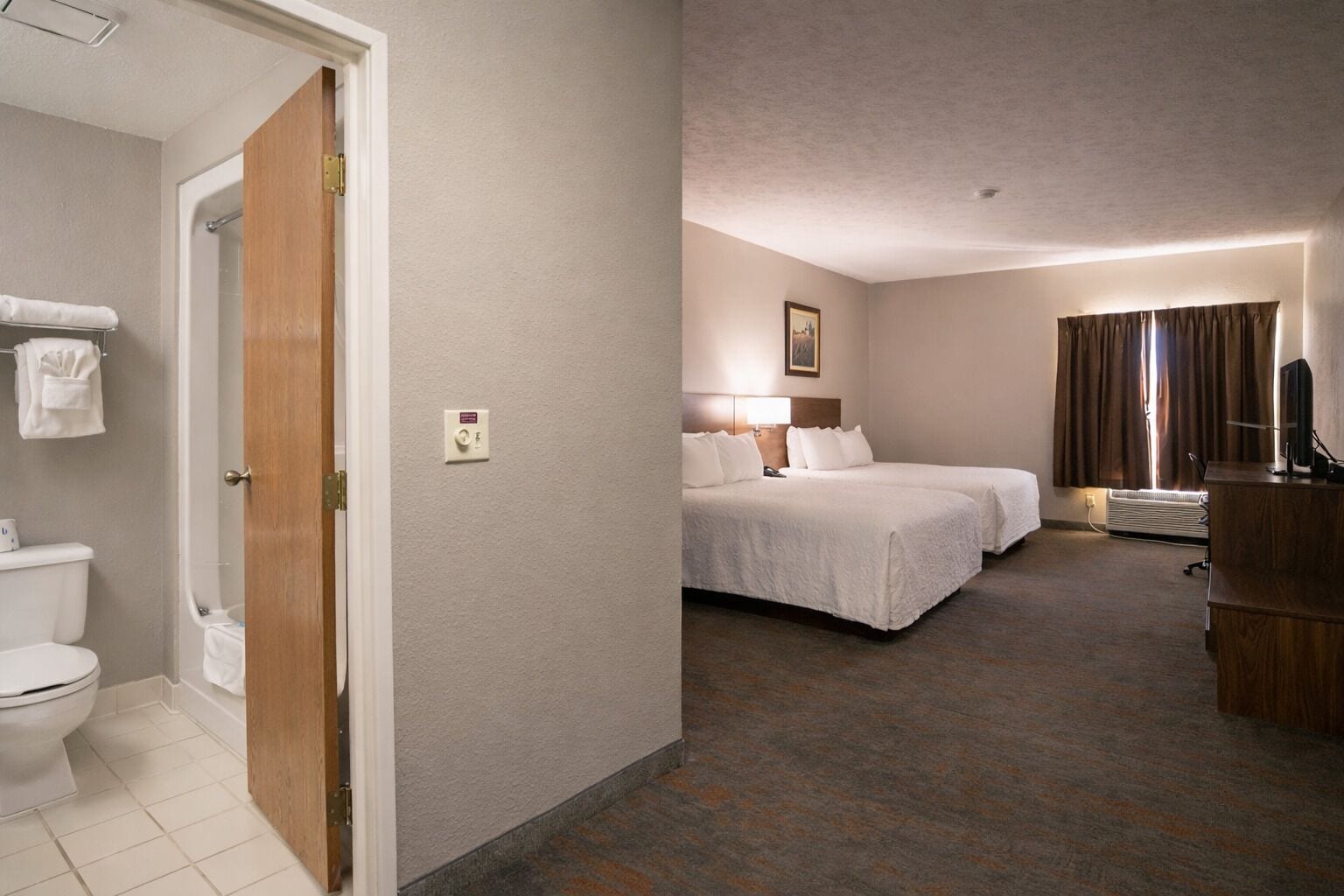 A hotel room with a toilet, two beds, a desk, and a television.
