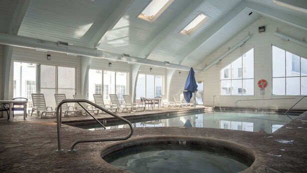 An indoor swimming pool with a stone floor, lounge chairs, and a covered area.