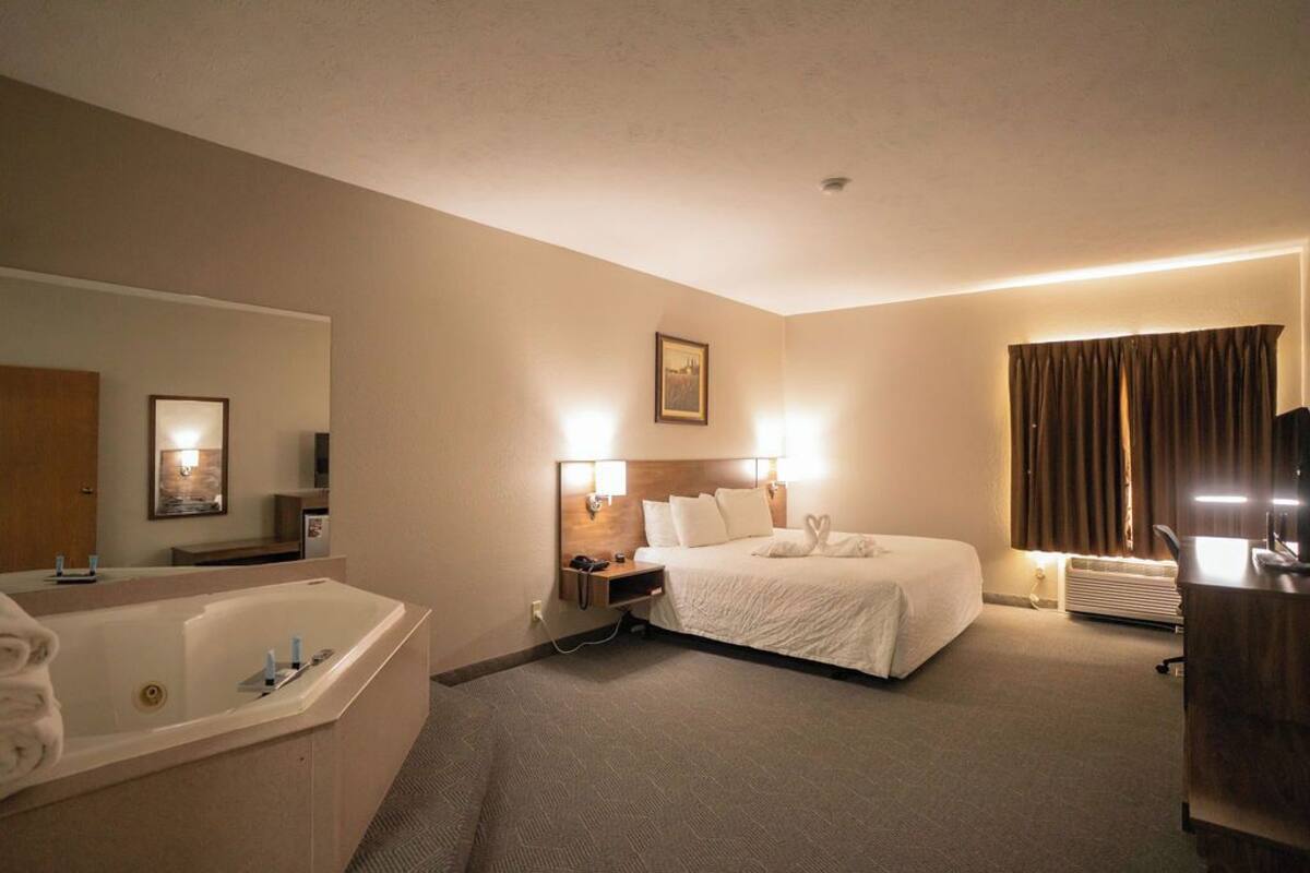 A hotel room with a large bed, a separate bathroom, a desk, and a large window with curtains.