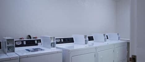 A laundry facility with multiple washing machines and dryers, a tiled floor, and fluorescent lighting.