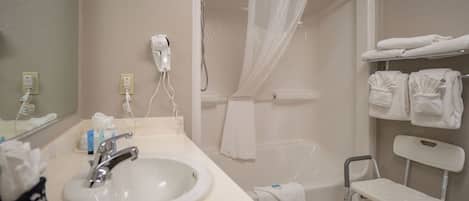 A bathroom with a sink, a shower with a curtain, a towel rack, and a step stool.