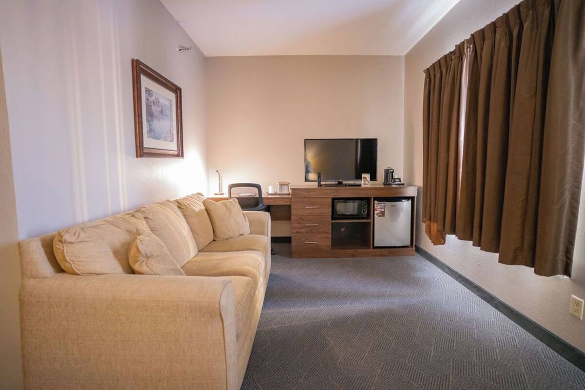 A hotel room with a sofa, a TV, a kitchenette, and curtains.
