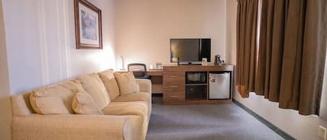 Una habitación de hotel con sofá, televisión, kitchenette y cortinas.