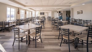 A spacious dining area with multiple tables and chairs, large windows, and a kitchen area in the background.