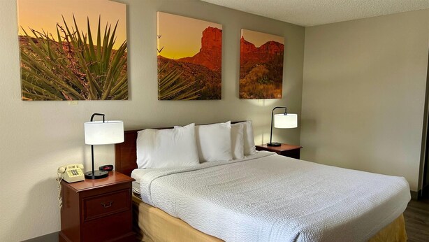 A hotel room with a bed, two bedside lamps, a nightstand with a phone, and three desert landscape paintings on the wall. - Days Inn by Wyndham Kingman West (Kingman)
