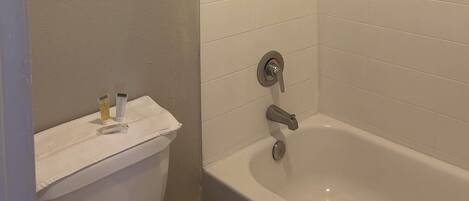 Et badeværelse med et hvidt toilet, et badekar og et håndklædestativ med toiletartikler.