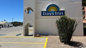 A Days Inn sign with a sun emblem, a parking lot, and a small cactus plant. - Days Inn by Wyndham Kingman West (Kingman)