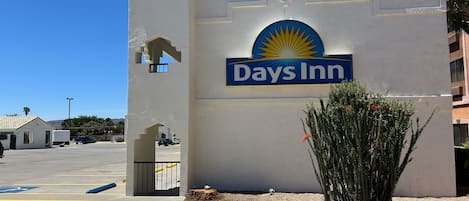 Señal de Days Inn con un emblema de sol, un estacionamiento y una pequeña planta de cactus.