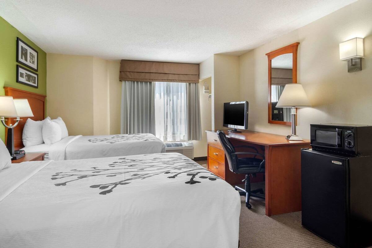 A hotel room with two beds, a desk with a computer, a microwave, and a refrigerator.