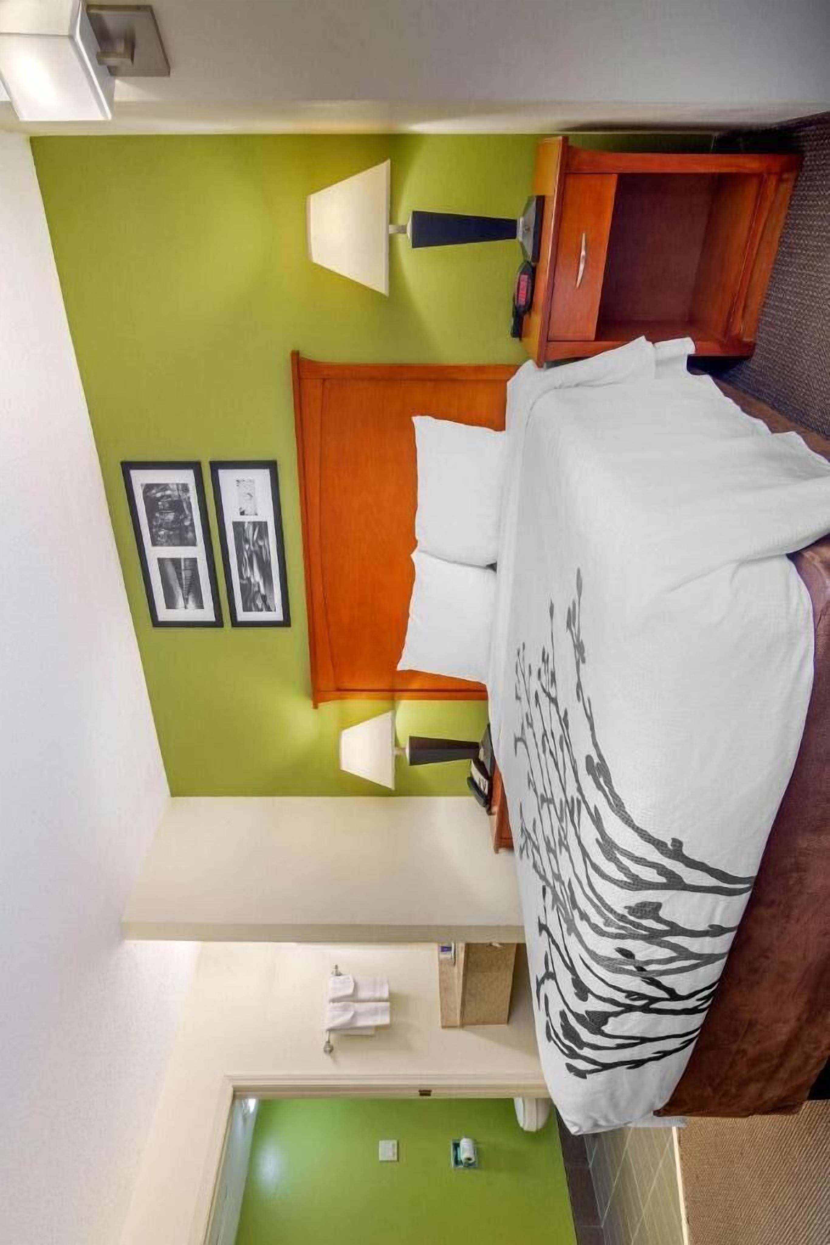 A hotel room with a bed, a nightstand, a lamp, a wooden wardrobe, and a green wall with framed pictures.