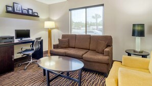 A hotel room with a sofa, a yellow armchair, a desk with a computer, a lamp, and a large window.