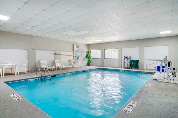 An indoor swimming pool with clear water, white lounge chairs, and a lifeguard stand.
