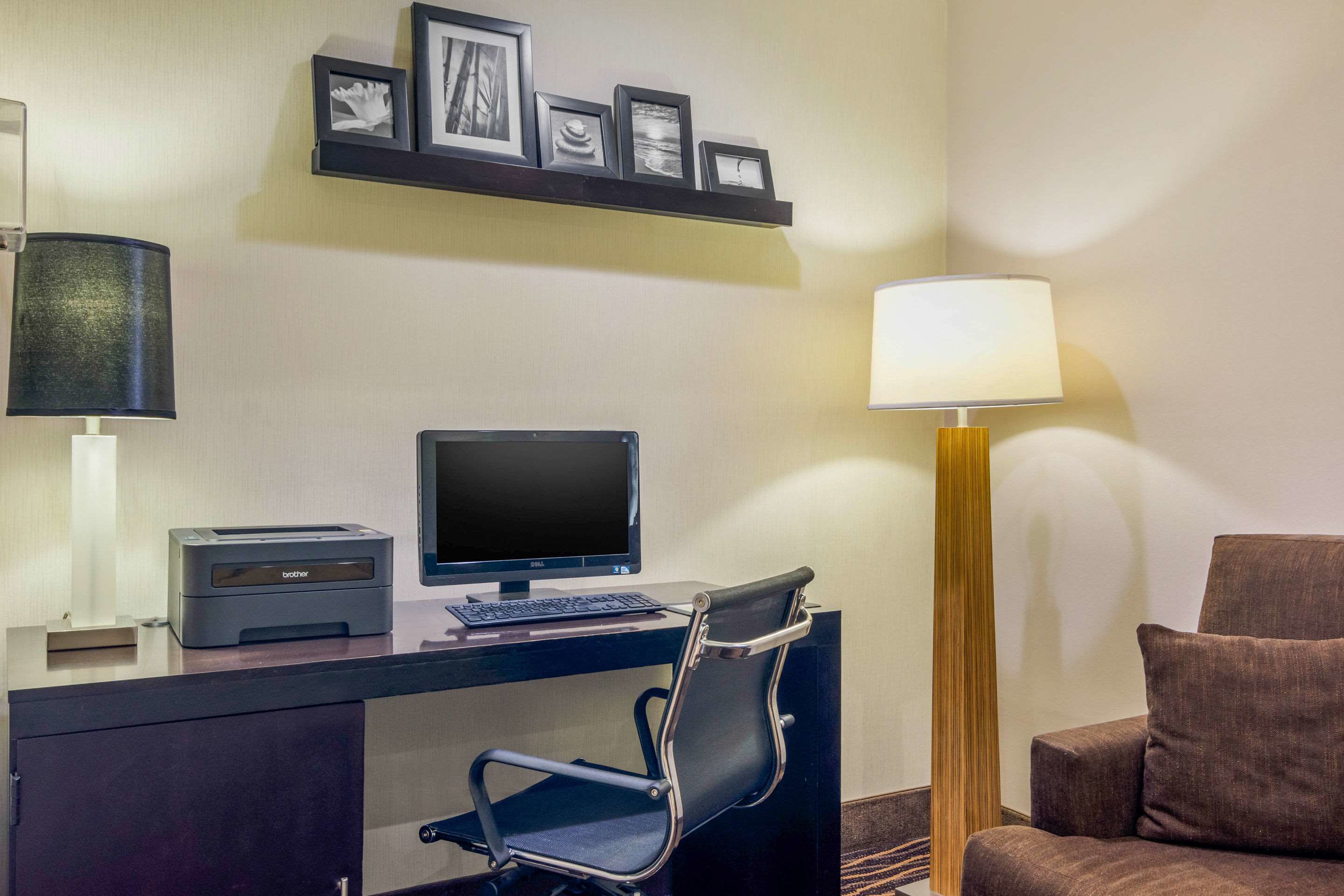 A hotel room with a desk, computer, printer, chair, lamp, and a couch.