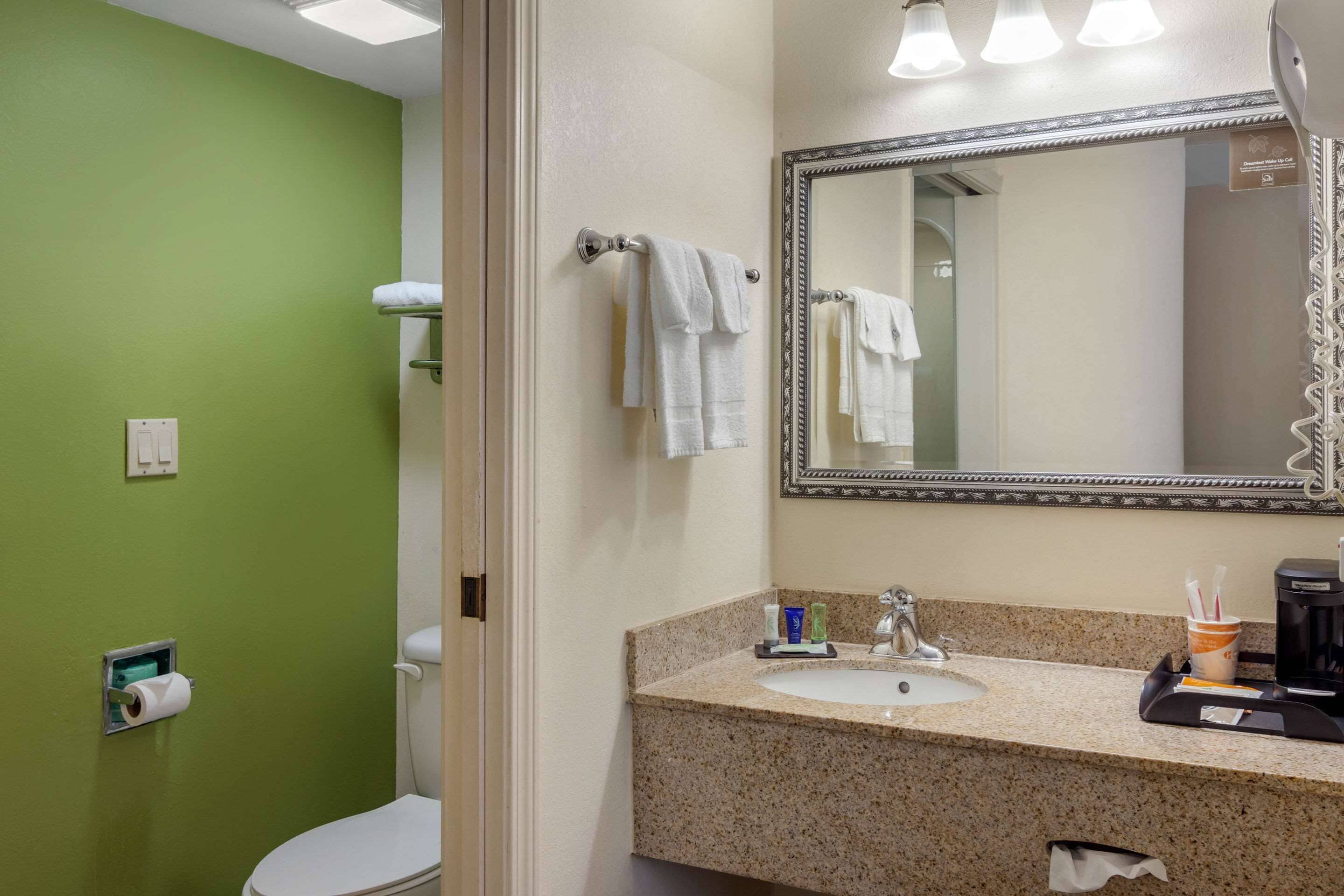 A bathroom with a green wall, a white toilet, a sink with a mirror, and a towel rack.