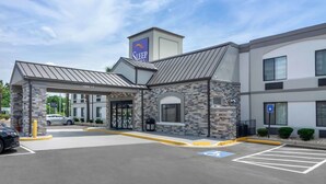 A hotel entrance with a stone facade, a clear sky, and a parking lot with marked handicapped spaces.