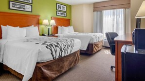 A hotel room with two beds, a desk, a chair, and a lamp.