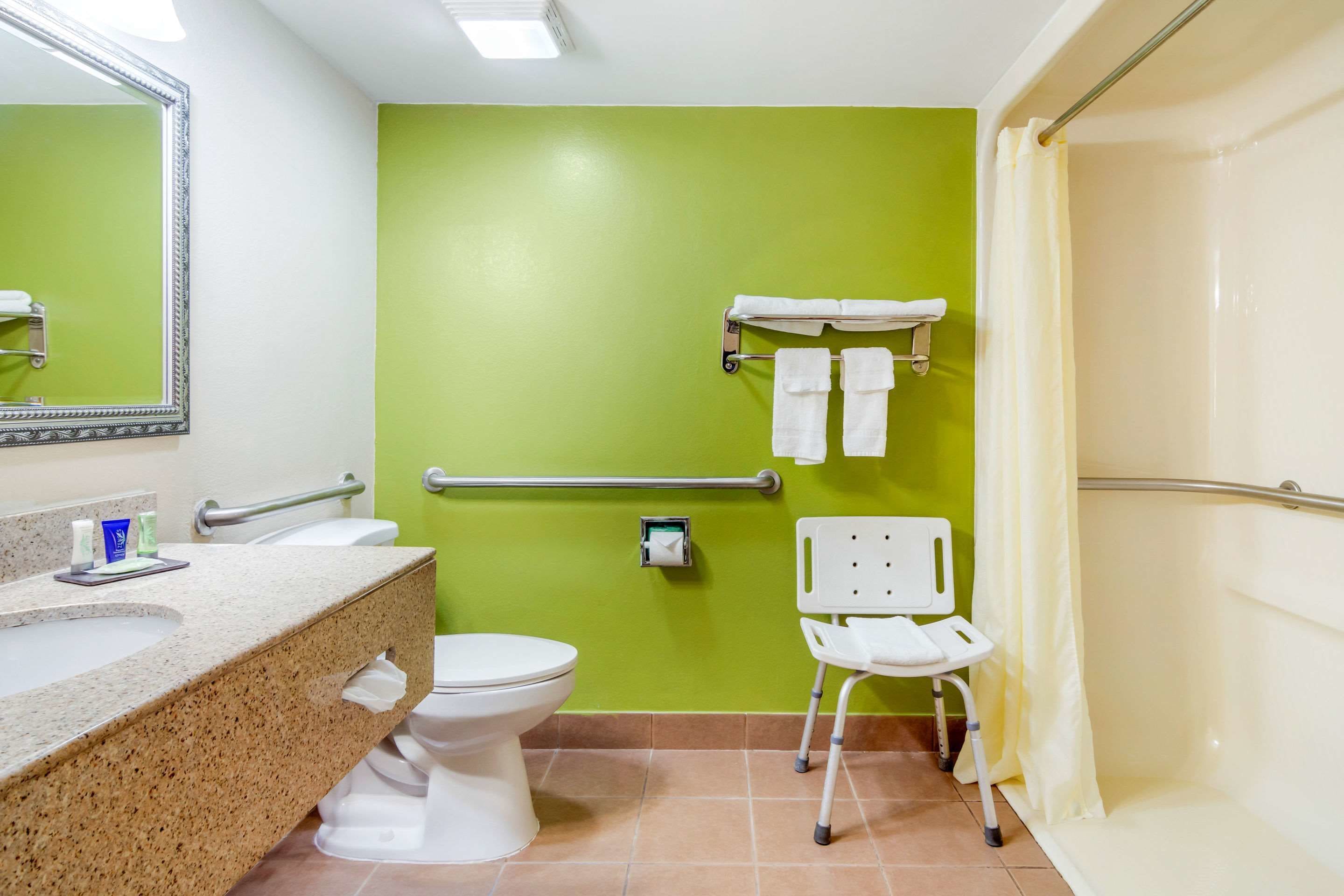 A bathroom with a green wall, white toilet, and a shower with a white chair.