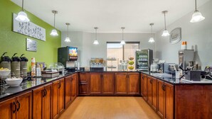 A modern kitchen with wooden cabinets, a black countertop, and various appliances. There are hanging lights, a coffee machine, and a refrigerator.