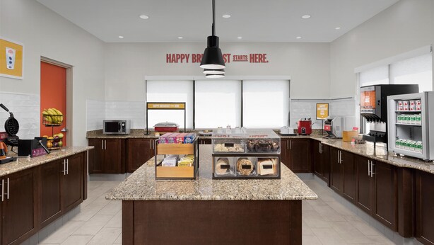 A modern kitchen with a central island, microwave, refrigerator, and various food items on the counter. - Hampton Inn Fayetteville Fort Bragg (Fayetteville)