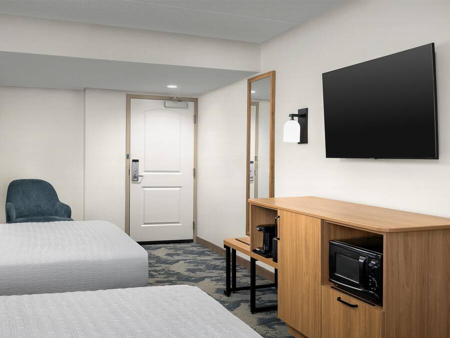 Een hotelkamer met twee bedden, een houten kastje met een magnetron, een stoel en een aan de muur bevestigde televisie.