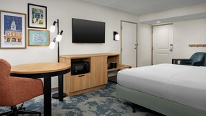 A hotel room with a bed, a desk with a microwave, a chair, a TV, and framed pictures on the wall. - Hampton Inn Fayetteville Fort Bragg (Fayetteville)