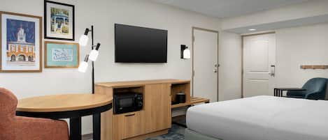 Ein Hotelzimmer mit Bett, Schreibtisch mit Mikrowelle, Stuhl, Fernseher und gerahmten Bildern an der Wand.
