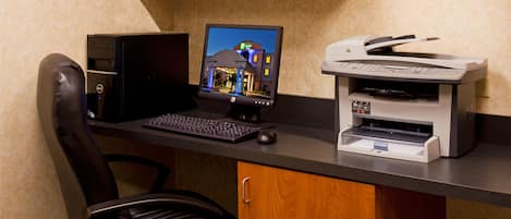 Un ufficio hotel con un computer desktop, una stampante e una poltrona in pelle.