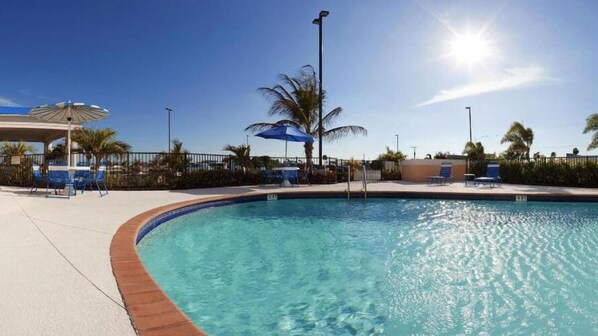 A swimming pool with clear blue water, surrounded by lounge chairs and umbrellas, under a sunny sky. - Holiday Inn Express Hotel & Suites Lake Okeechobee by IHG (Okeechobee)