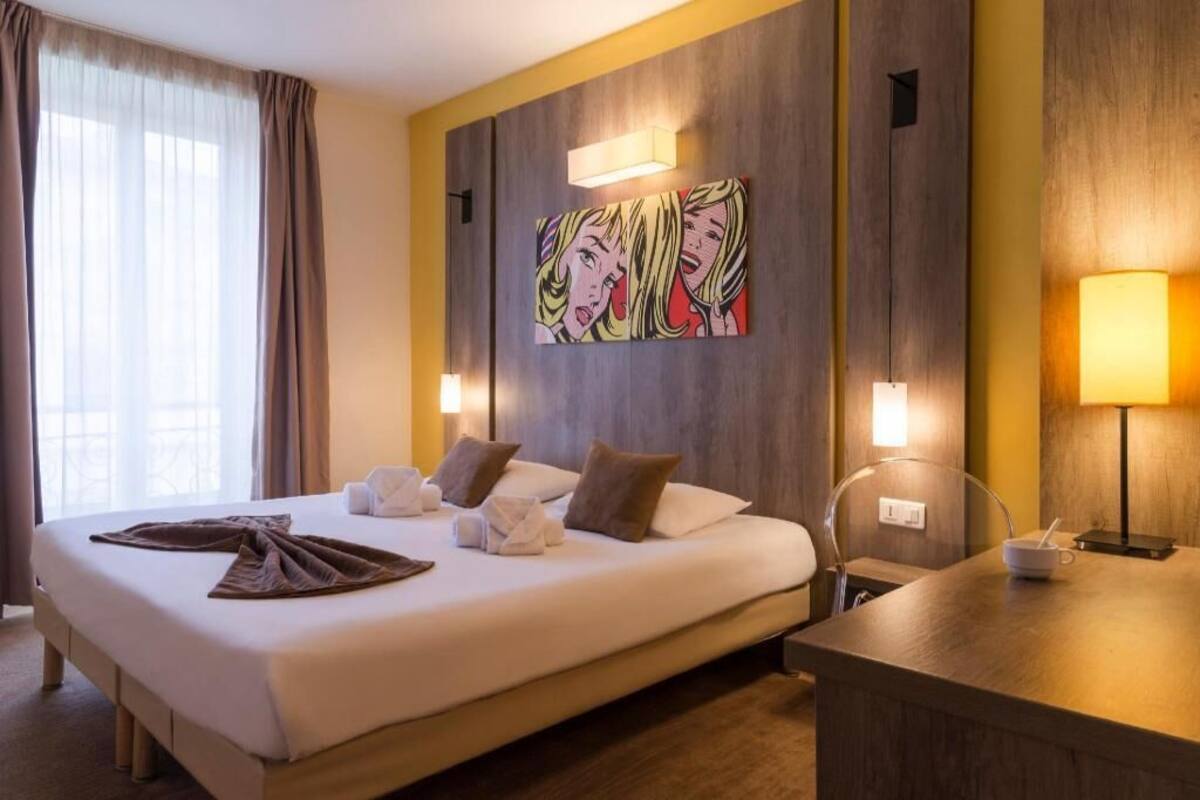 Une chambre d’hôtel avec un grand lit, des lampes de chevet, un tableau au mur et un bureau avec une lampe.