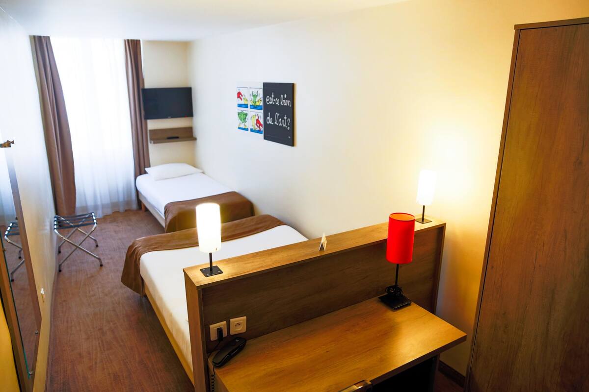 Une chambre d’hôtel avec deux lits, un bureau, une chaise, une télévision et une œuvre d’art accrochée au mur.