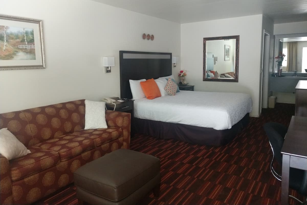 A hotel room with a bed, a sofa, an ottoman, a nightstand, a mirror, and a desk.