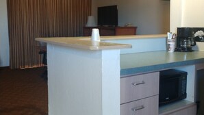 A small kitchenette with a microwave, coffee maker, and a cup holder. There is a television and a curtain in the background.