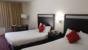 A hotel room with two beds, a desk, a chair, a lamp, and a telephone.