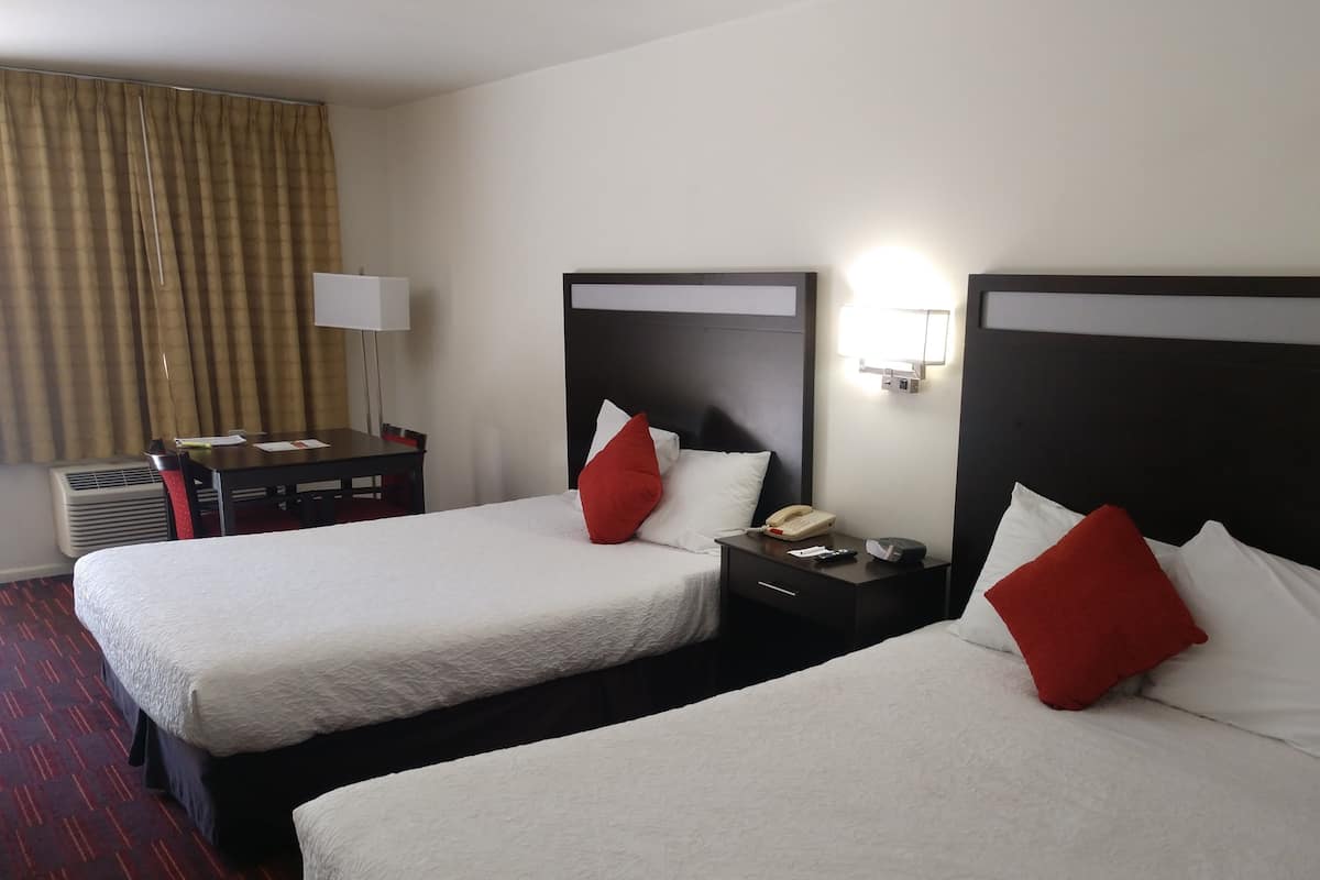 A hotel room with two beds, a desk, a chair, a lamp, and a telephone.