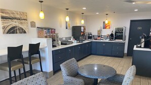 Een moderne keuken met donkerblauwe kastjes, een centraal eiland en een zithoek met patroontekening stoelen en een ronde tafel.