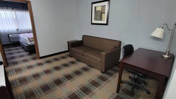 A hotel room with a bed, a sofa, a desk, and a lamp.