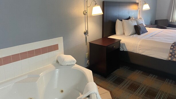 Een hotelkamer met een groot bed, een nachtkastje, een badkamer met een bad en twee wandlampen.