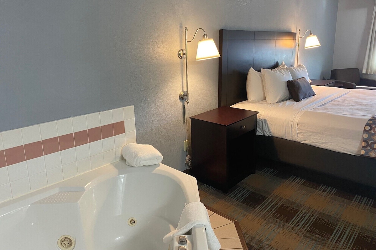 A hotel room with a large bed, a nightstand, a bathroom with a bathtub, and two wall-mounted lamps.