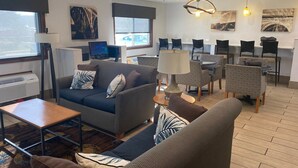 Een moderne woonkamer met een bank, fauteuils, een salontafel en een eethoek met stoelen. Er is een televisie, een lamp en kunstwerken aan de muur.