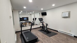 Een fitnessruimte met een loopband, hometrainer en trainingsapparatuur.