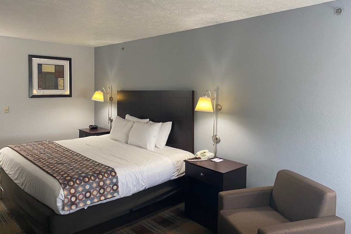 A hotel room with a large bed, two bedside lamps, a chair, a nightstand, and a framed picture on the wall.